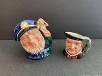 Two Royal Doulton Toby character mugs: Old Salt with a sailor hat and mermaid handle, Henry VIII with a traditional cap.