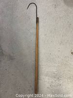 Full view of the antique fish hook showing the wooden handle and the hooked metal end.