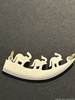 White elephant necklace pendant with three elephants carved along a curved tusk shape, photographed on black background.