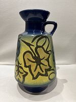 Front view showing yellow background with black outlined floral designs on blue base and rim