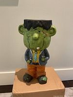 Front view of the green Frankenstein plaster figure with cartoon proportions, showing facial details and clothing.