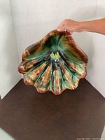 Large clam shaped pottery dish shown upright with hand holding for scale, showing detailed glaze and scalloped shape.