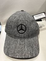 Front view of grey tweed golf hat with Mercedes-Benz black embroidered logo and attached tags.