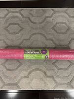 Photo showing the rolled, shrink-wrapped pink yoga mat on a patterned rug.