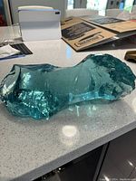 Close-up side view of the heavy aquamarine glass piece on a kitchen counter showing its thickness and color.