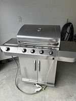 Full front view of closed stainless steel grill showing four control knobs, cabinet doors, and attached side shelves