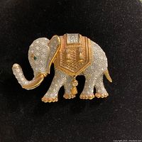 Front view of the elephant brooch highlighting the gilt metal, textured metal body, diamant and emerald crystals, pearl-like stone on trunk tip, and pendant charm.