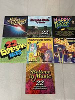 Top view of all seven K-Tel vinyl record sleeves arranged on floor, showing album titles and colorful vintage artwork.