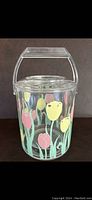 Front view of lucite ice bucket showing colorful tulip flowers painted on the exterior, clear handle on top.