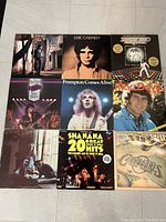 Nine vinyl records arranged in three rows, including Eric Carmen, Frampton Comes Alive, Mac Davis, Shanana's 20 Great Hits, Commodores, and Saturday Night Fever soundtrack.