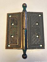 Close-up top view of one large brass door hinge showing embossed floral and geometric patterns with decorative pins and patina.