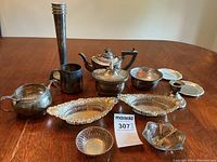Full lot of antique silver plated items displayed on wooden table including teapot, creamer, sugar bowl, trays, bowl with tongs, candlestick, vase, mug, plates