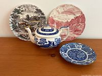 Front view of the set with the teapot centered and plates arranged behind and to side on wooden surface against white backdrop.