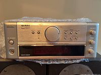 Front view of Denon UDRA-M10 receiver showing controls and display screen on silver faceplate.