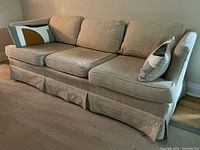 Three seater beige fabric sofa with three seat cushions and three down filled back cushions, two decorative pillows with geometric color block patterns. Scratches visible on sides, otherwise in good condition.