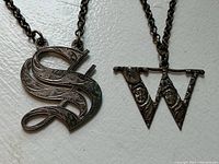 Photo of two English sterling silver decanter labels, one 'S' and one 'W', showing engraved details and attached chains.