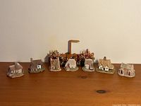 Wide view showing 7 miniature houses and a floral street sign arranged on a wooden surface.
