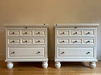 Front and slightly angled view of the pair of white antique style end tables, showing the drawer arrangement and bun feet.