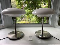 Front view of two table lamps on a windowsill showing chrome bases and white glass shades.