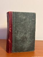 Front cover of antique book with dark green cloth and red leather spine showing wear.
