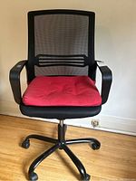 Front view showing black mesh backrest, red cushioned seat, armrests, and wheelbase on hardwood floor.