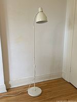 Full view of the vintage off white metal standing floor lamp with flexible goose neck and round base against a plain wall.