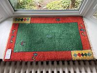 Full view of vintage Gabbeh style floor mat measuring approximately 36x22 inches with green central field and red borders, placed in front of a window.