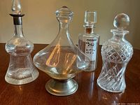 Four vintage glass decanters shown side by side against a plain background each with distinct features including the metal accented tops and stand