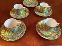 Photo showing four tea cups placed on their matching saucers, with two additional tea plates in the background, all featuring the green floral chintz pattern.