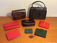Wide shot showing all eight items on wooden surface: two handbags and six wallets in brown, black, red, and green leather.