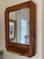 Full view of vintage pine wood framed wall mirror with bottom shelf showing it hanging on wall next to a door with decorative glass.
