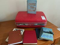 Vintage red Samsonite hard suitcase with five notebooks arranged in front and one standing on top.
