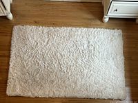 White faux fur area rug laid flat on wooden floor, displaying full rectangular size and shaggy texture.