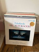 Stack of vinyl record albums with Tchaikovsky The Nutcracker suite visible on top, placed on wood floor along wall