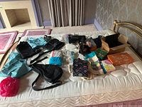 Lot spread on bed showing garment bags in black and blue, cardboard boxes, diapers, security bars, and various small items including packing materials.