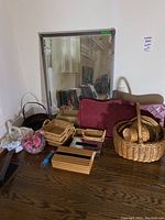 Photo of several wicker baskets, two burgundy facial tissue covers, a small plastic tray, and a large rectangular mirror leaning against the wall.