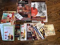 Top view of the cookbooks stacked on a wooden floor, showing various colorful covers and titles.