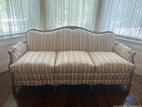 Front view of antique wood frame couch with floral striped upholstered cushions, showing carved wooden top rail and padded armrests.