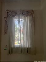Curtain set with linen sheers and taffeta valences on a window, light filtering through the sheer panel, with swag valence draped atop.