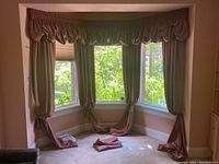 Window corner with four mauve colored curtain panels hanging long and three valence pieces above windows.