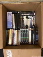 Photo showing a box of VHS tapes including titles like Les Misérables, Star Wars, and others mostly in plastic VHS cases.