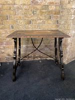 Full side view of the carved wood top table with metal legs against a brick wall background.
