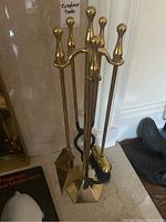 Photo showing brass fireplace tools on stand with ball handles and hexagonal base, positioned by a fireplace.