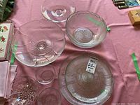 Top view of six clear glass items on a pink cloth including various platters, bowls, and plates with different textures and designs.