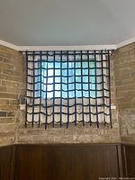 Photo of a square window with a black leather grid-style blind mounted inside a brick wall.
