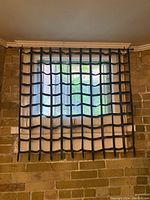 Full view showing one leather blind mounted on a window with brick wall background, black leather grid design