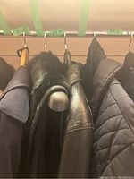 Photo showing multiple clothing items on hangers including the leather jacket and the fur knit vest.
