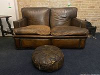 Front view of brown leather love seat with down-filled cushions and matching round ottoman