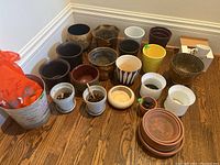 Wide view showing an assortment of 21 planters in various materials and sizes grouped on a floor corner.