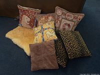 Set of seven decorative cushions arranged with a natural cream sheepskin throw on dark blue carpet.
